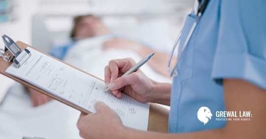 Doctor writing on a clipboard with a patient lying in a hospital bed in the background.